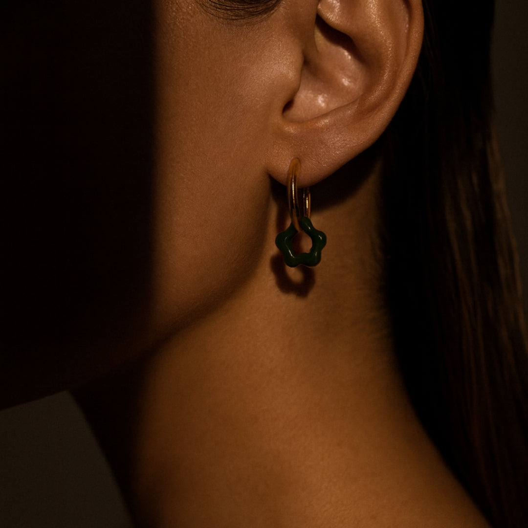 Close-up of an ear wearing a gold hoop earring with a green stone against a dark background