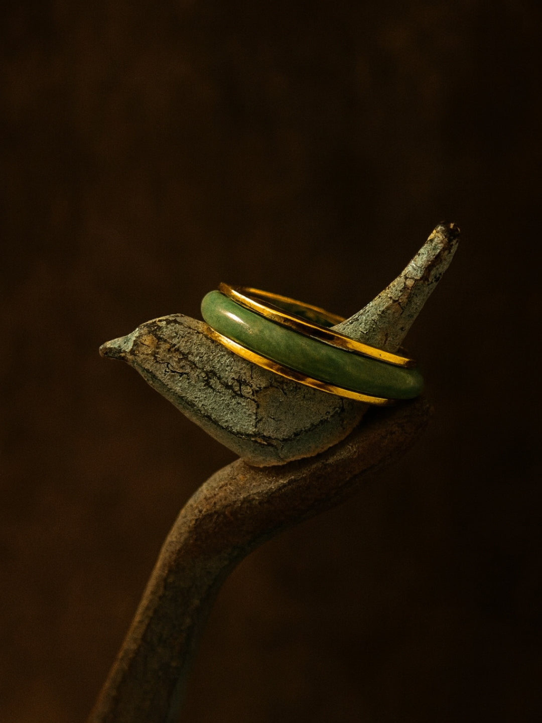 Green jade ring with gold band on a textured surface