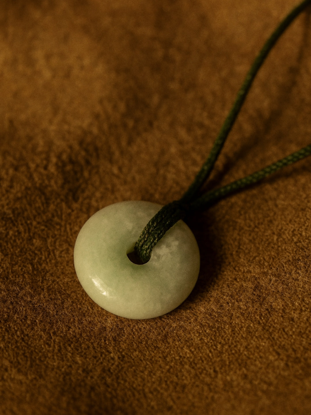 Round jade pendant on a green cord against a brown background
