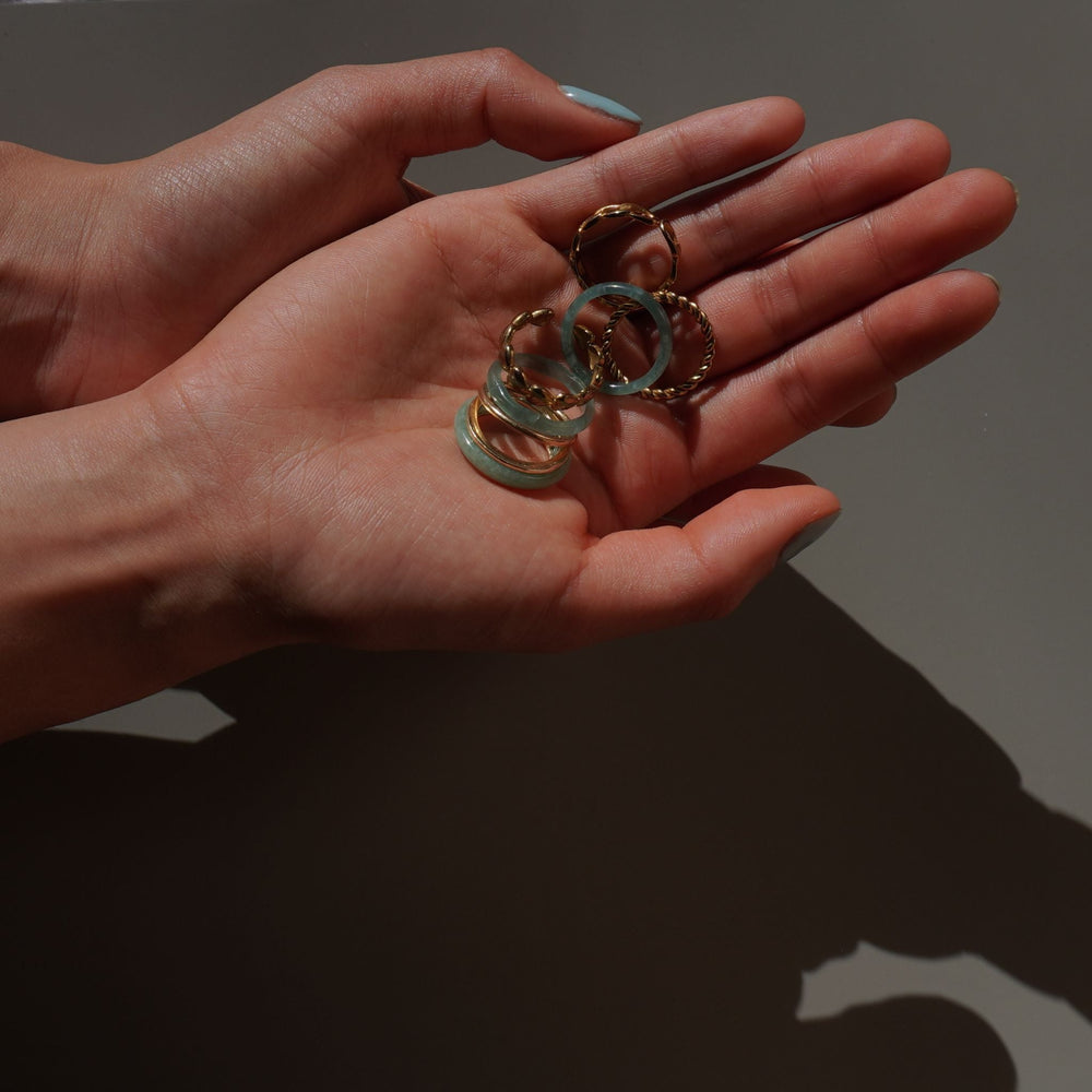 Hand showcasing an elegant everyday ring stack with solid gold bands and natural jade rings from Aulyn.