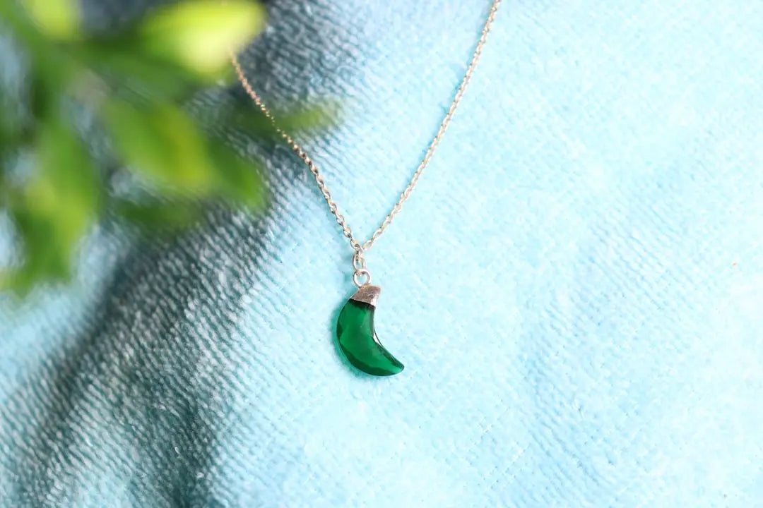 A green horn pendant hangs on a delicate chain. - Photo by Sahil Kumar on Unsplash