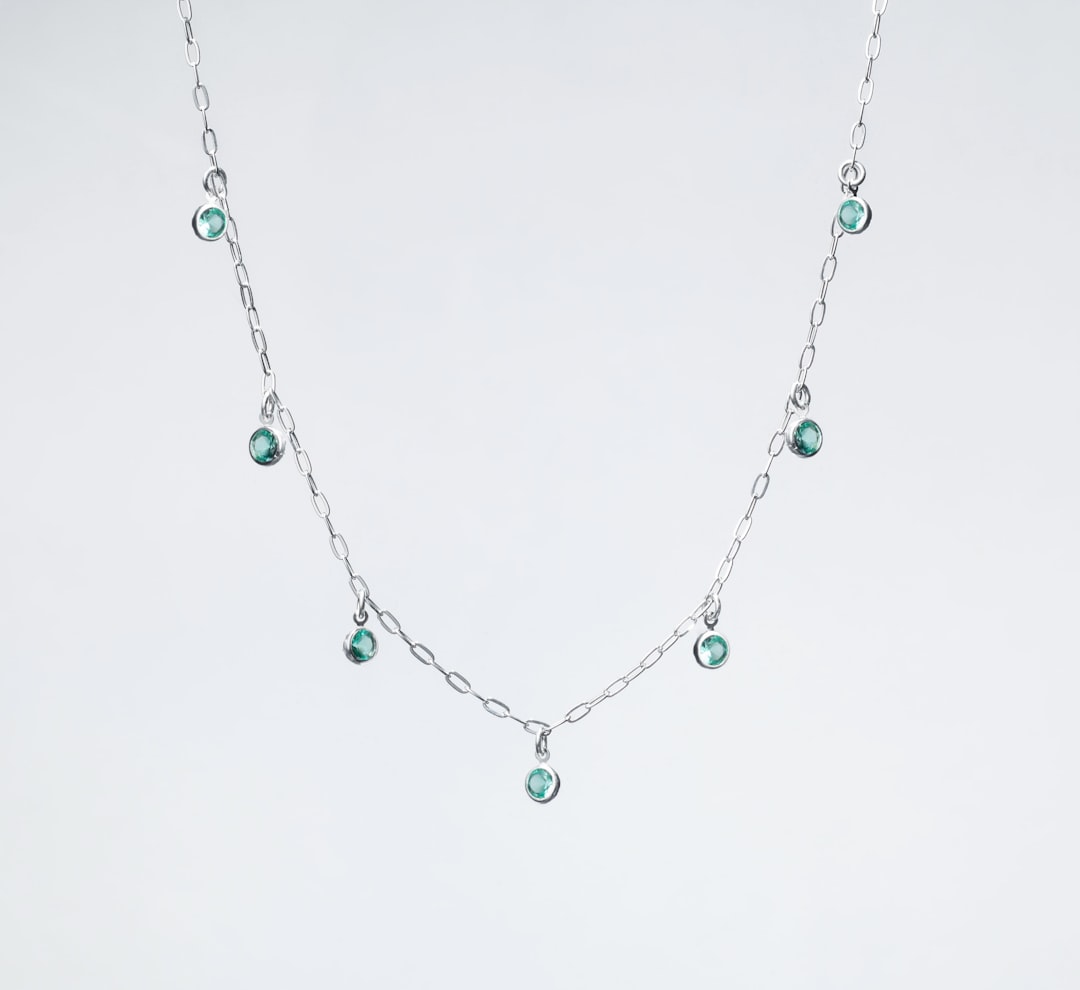 a silver necklace with green beads on a white background - Photo by Ian Talmacs on Unsplash