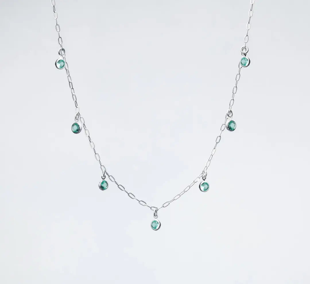 a silver necklace with green beads on a white background - Photo by Ian Talmacs on Unsplash