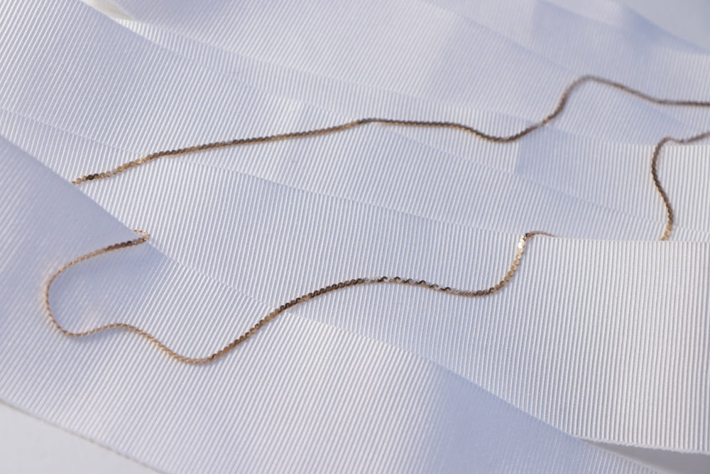 A gold chain lies on white fabric. - Photo by R. G on Unsplash