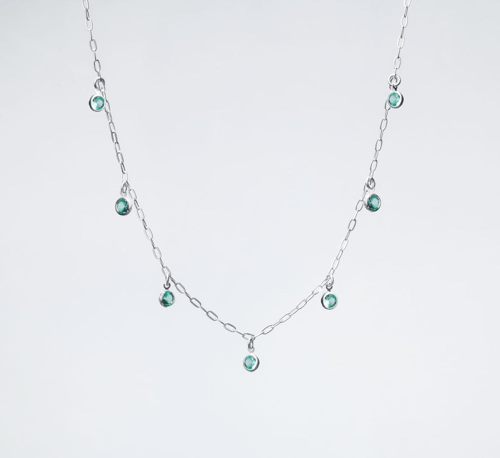 a silver necklace with green beads on a white background - Photo by Ian Talmacs on Unsplash