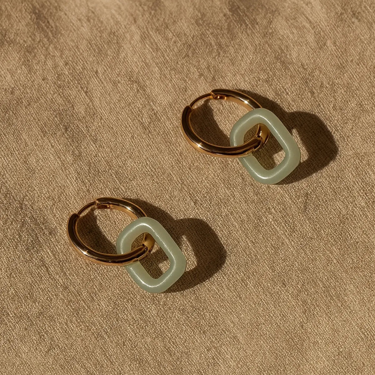 Pair of gold hoop earrings with green jadeite links, styled on olive background – Jaura Earrings by Aulyn