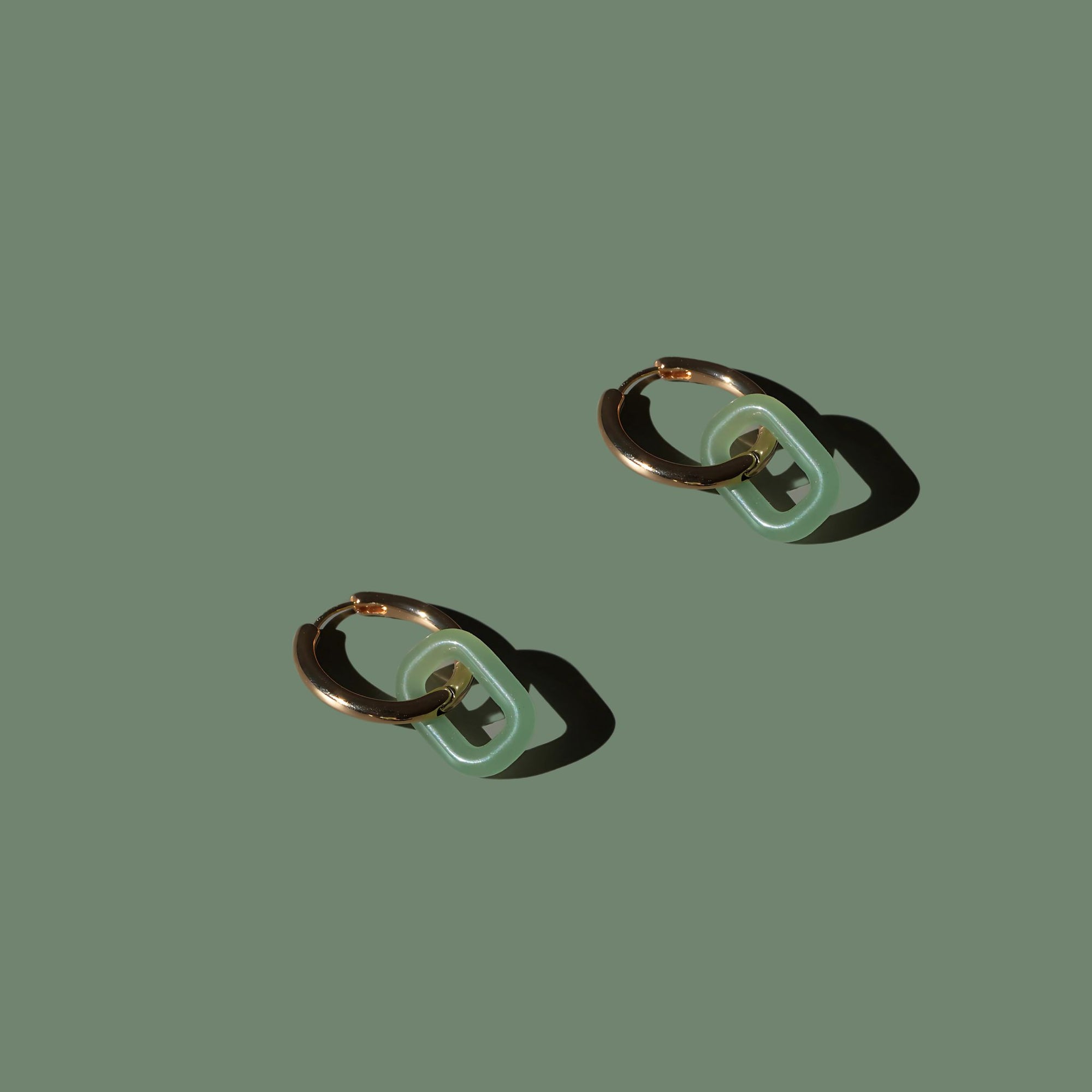 Pair of gold hoop earrings with green jadeite links, styled on olive background – Jaura Earrings by Aulyn