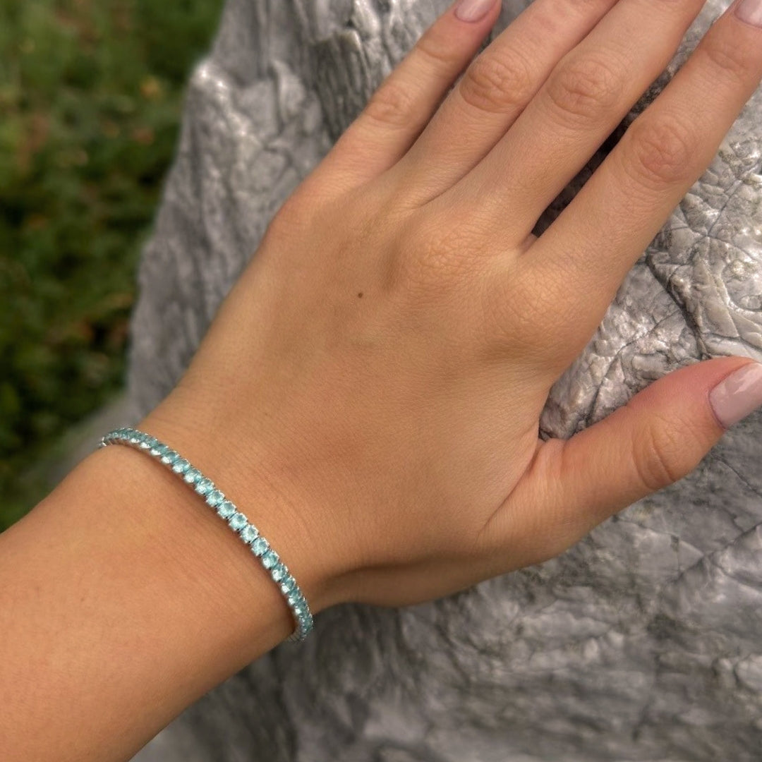 Hand wearing a blue beaded bracelet against a stone wall background