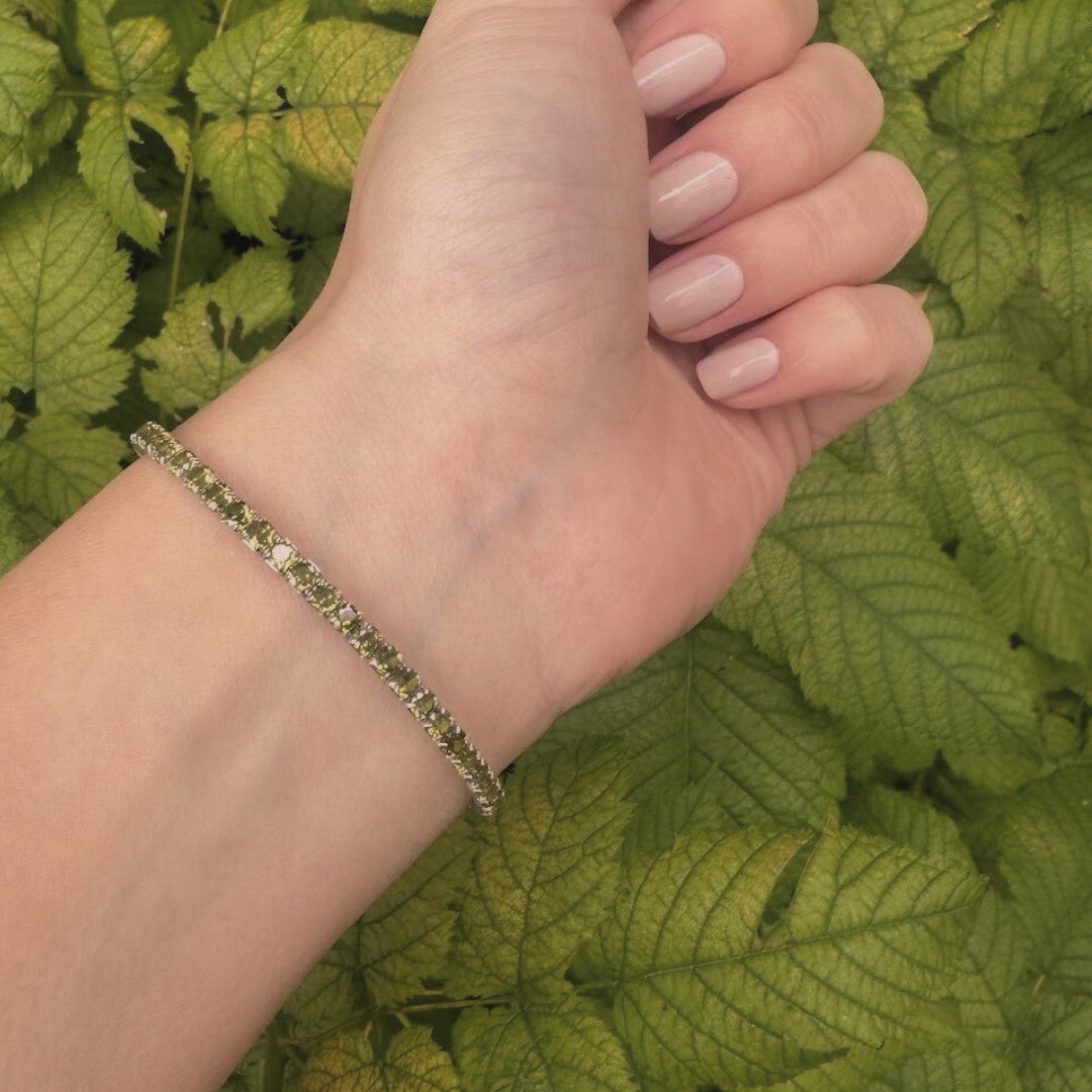 Hand wearing a bracelet with green leaves in the background