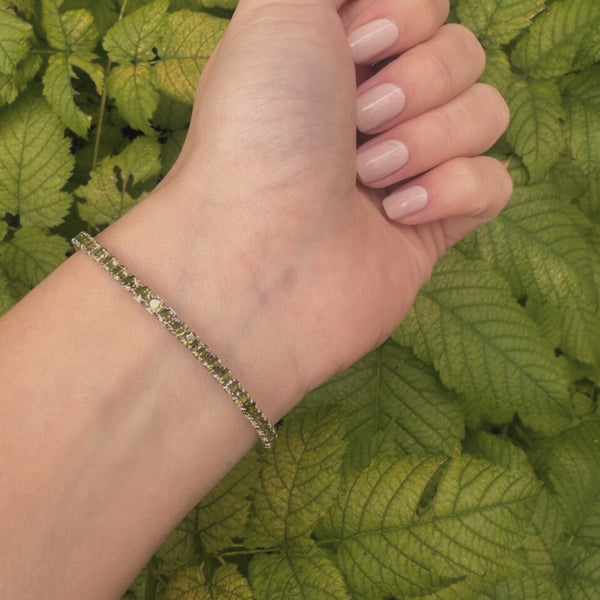 Hand wearing a bracelet with green leaves in the background