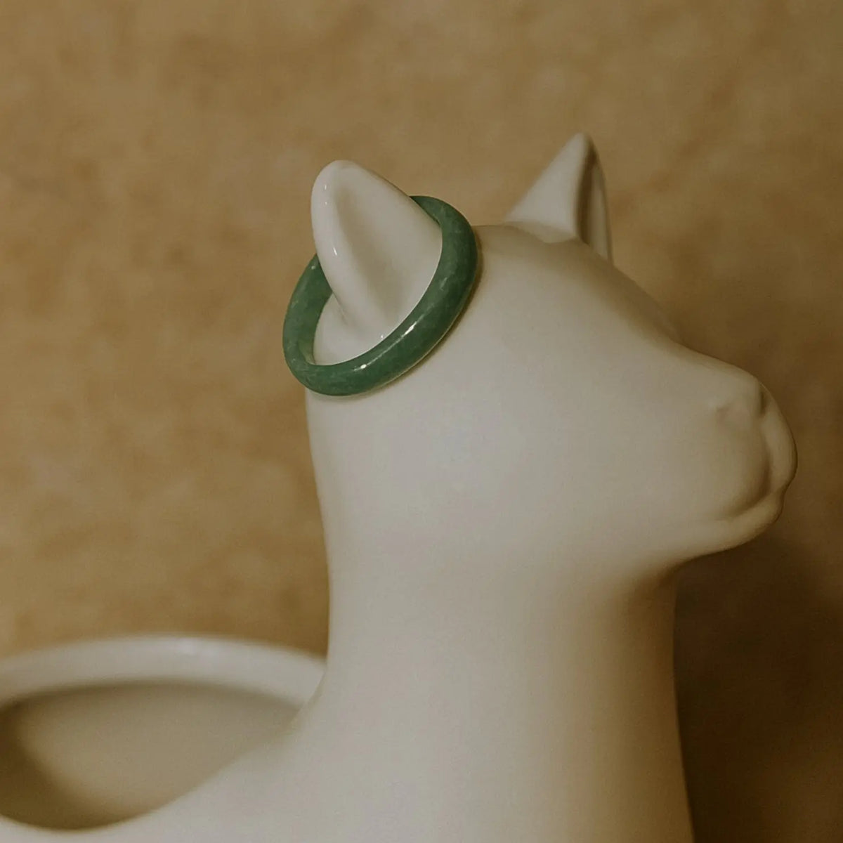 Light green Jade ring on white ceramic cat jewelry holder, minimalist product display on green background.