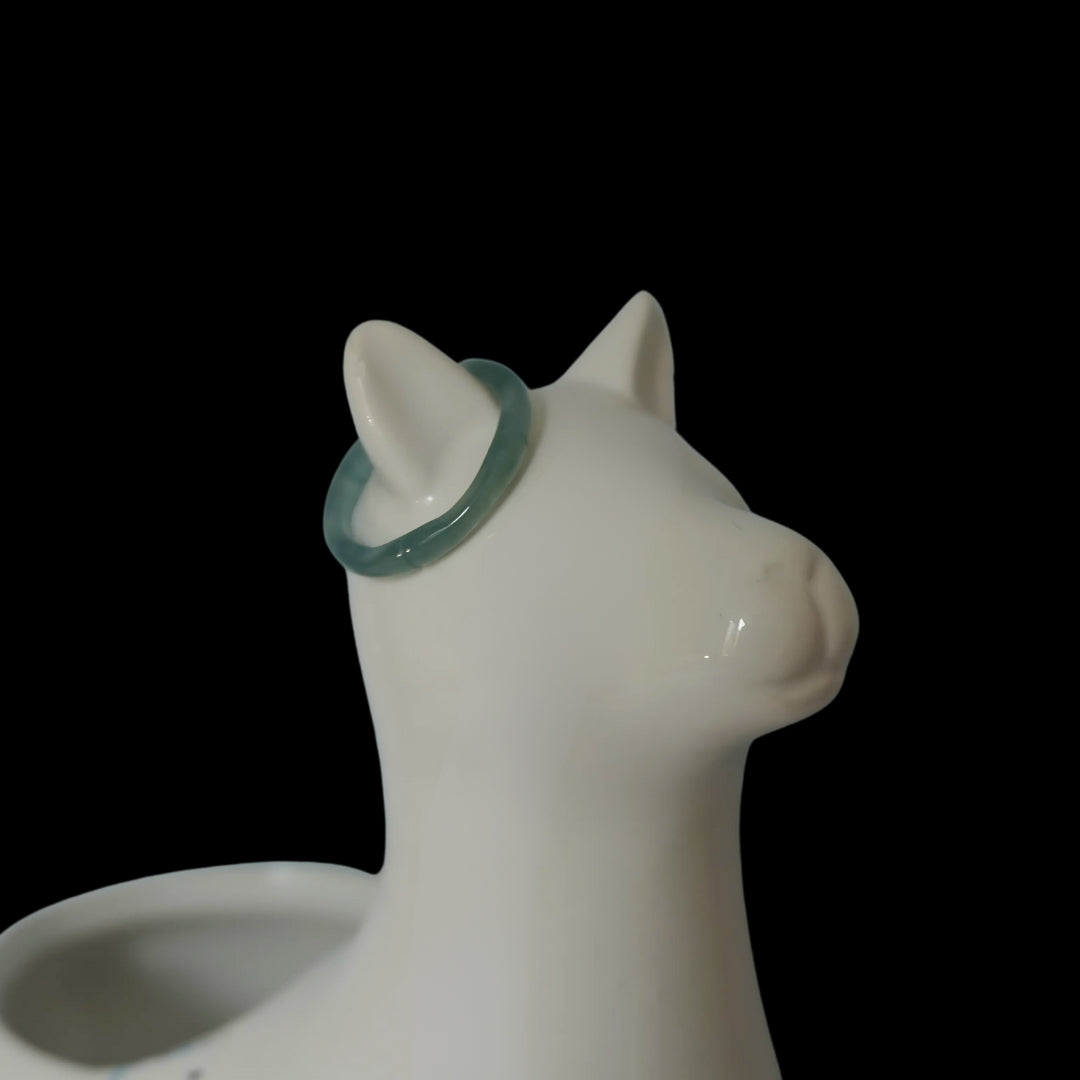 Light green Luwen Jade ring on white ceramic cat jewelry holder, minimalist product display on black background.