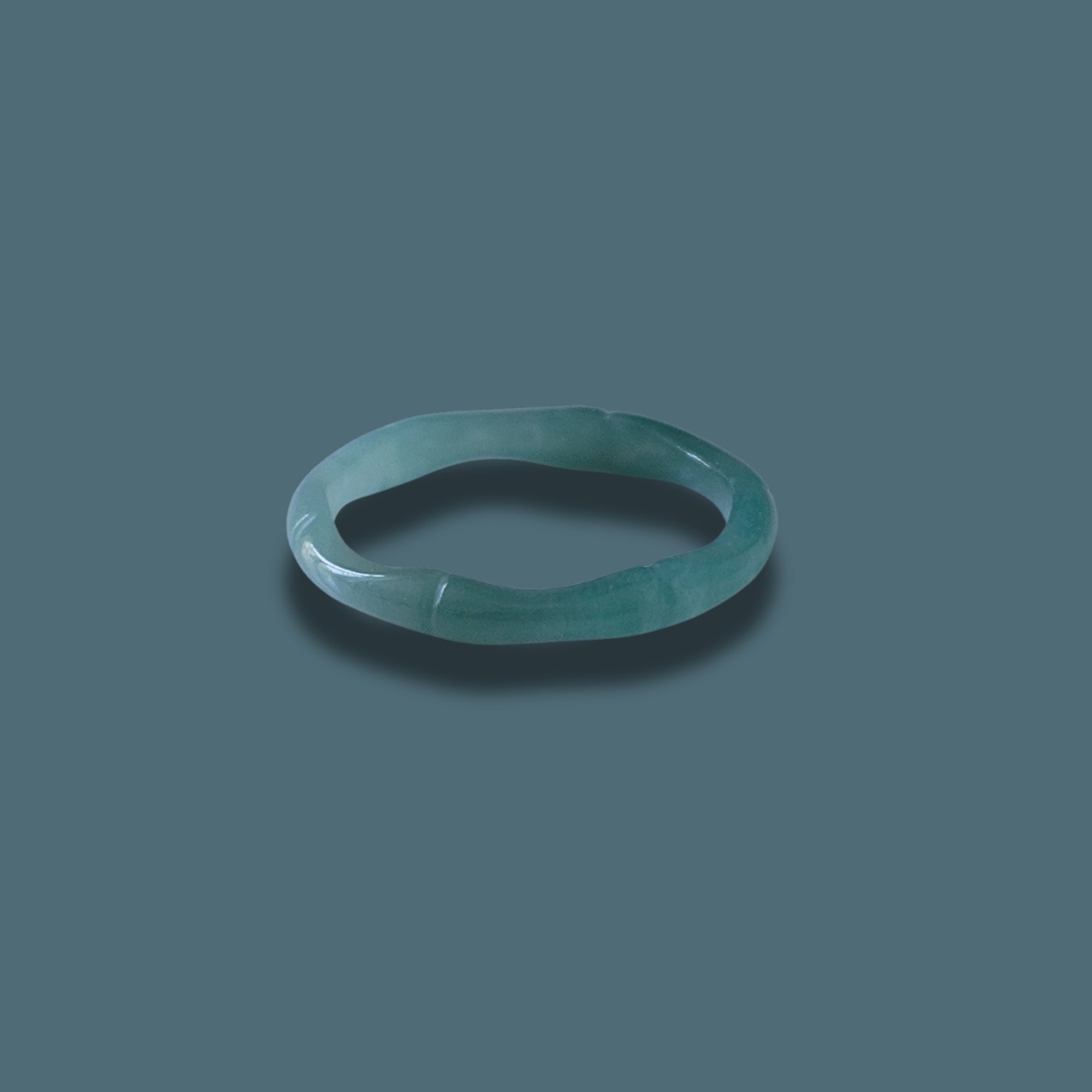 Elegant green Jadeite ring with detailed carvings, displayed on a dark green background.