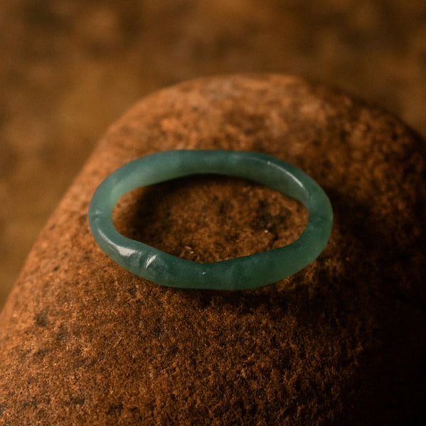 Elegant green Jadeite ring with detailed carvings, displayed on a dark green background.