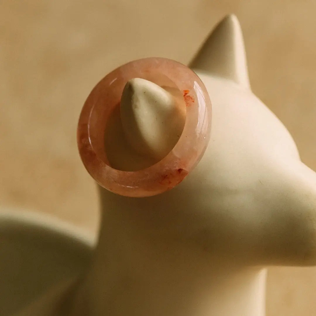 Light Ping Meihua ring on white ceramic cat jewelry holder, minimalist product display on pink background.