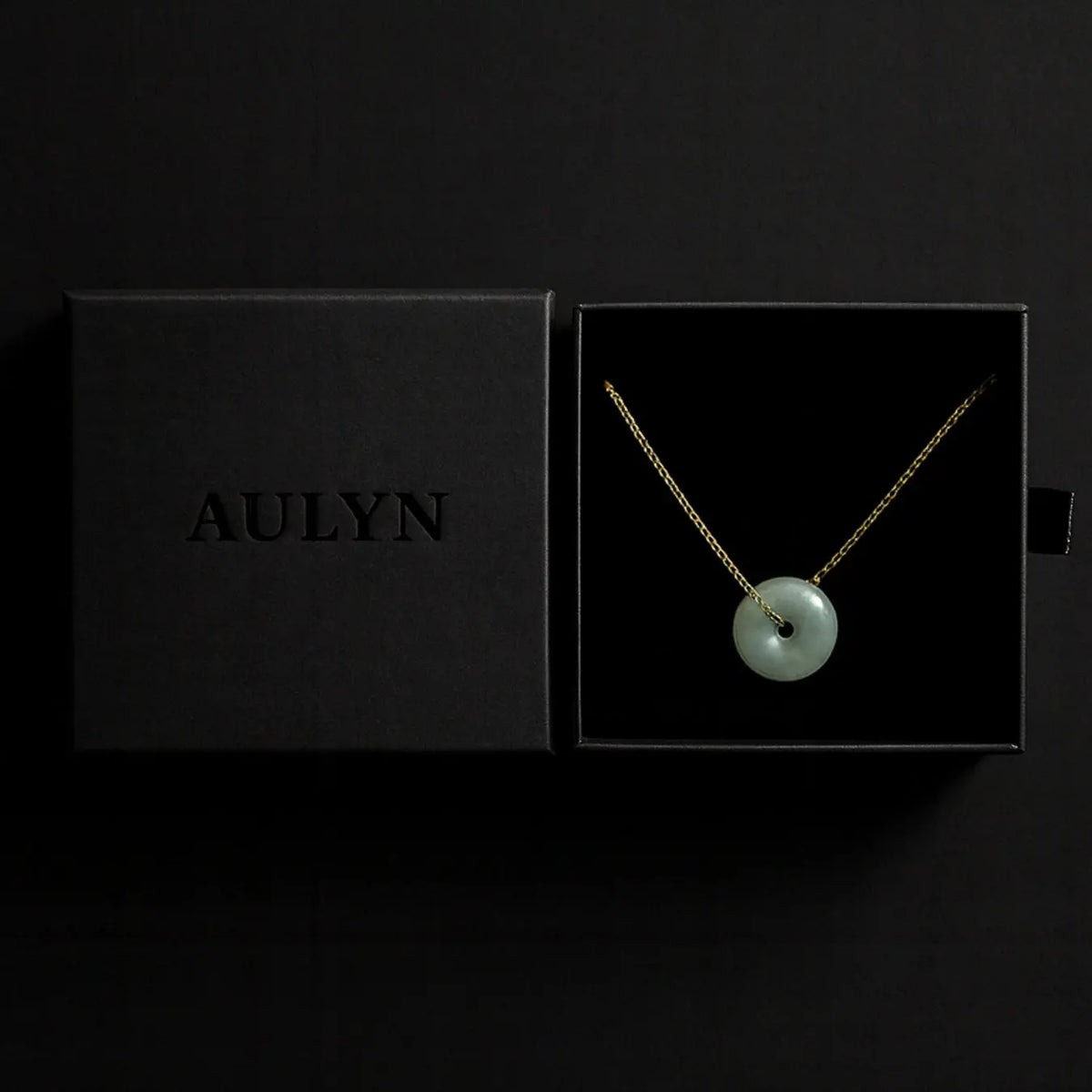Necklace with a green pendant in an open black box displaying the brand 'AULYN'.