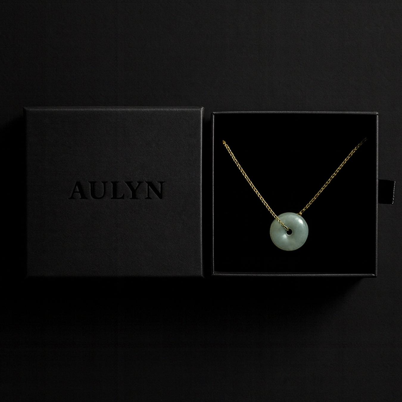 Necklace with a green pendant in an open black box displaying the brand 'AULYN'.
