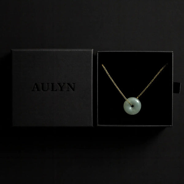 Necklace with a green pendant in an open black box displaying the brand 'AULYN'.