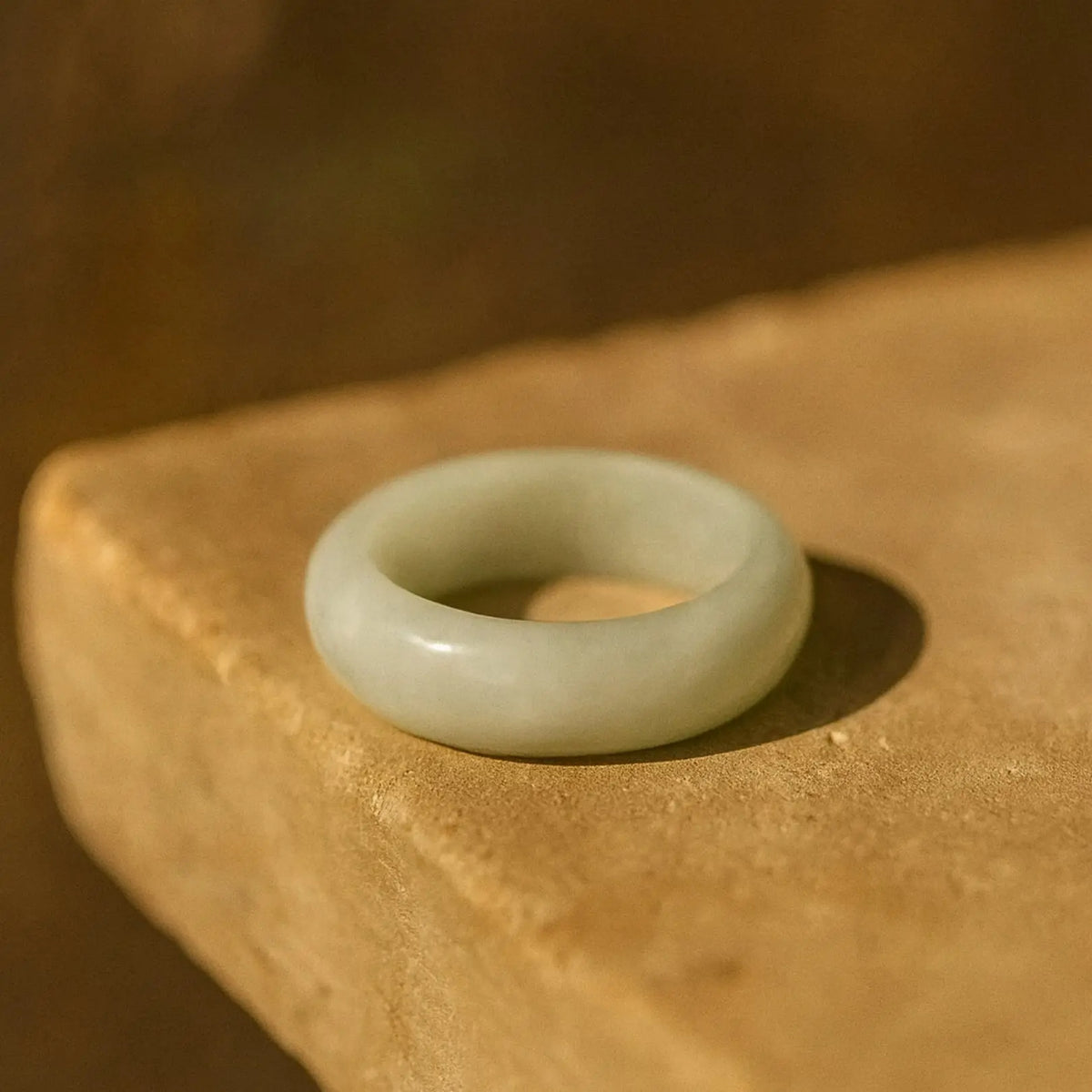 White jadeite ring (Nivelle Ring) displayed on a soft green background, highlighting its smooth, polished surface and minimalist design.