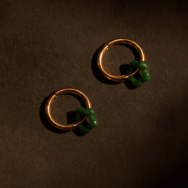 Gold hoop earrings with green beads on a dark brown background