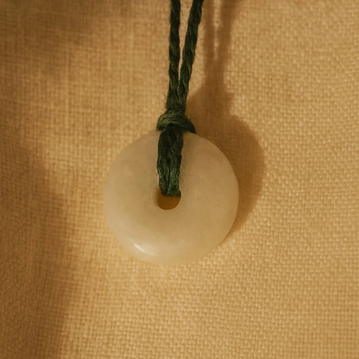 White circular pendant with green cord on a beige textured background