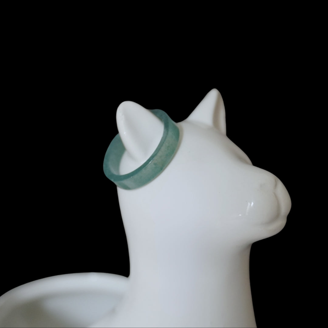 Light green Seren Jade ring on white ceramic cat jewelry holder, minimalist product display on black background.