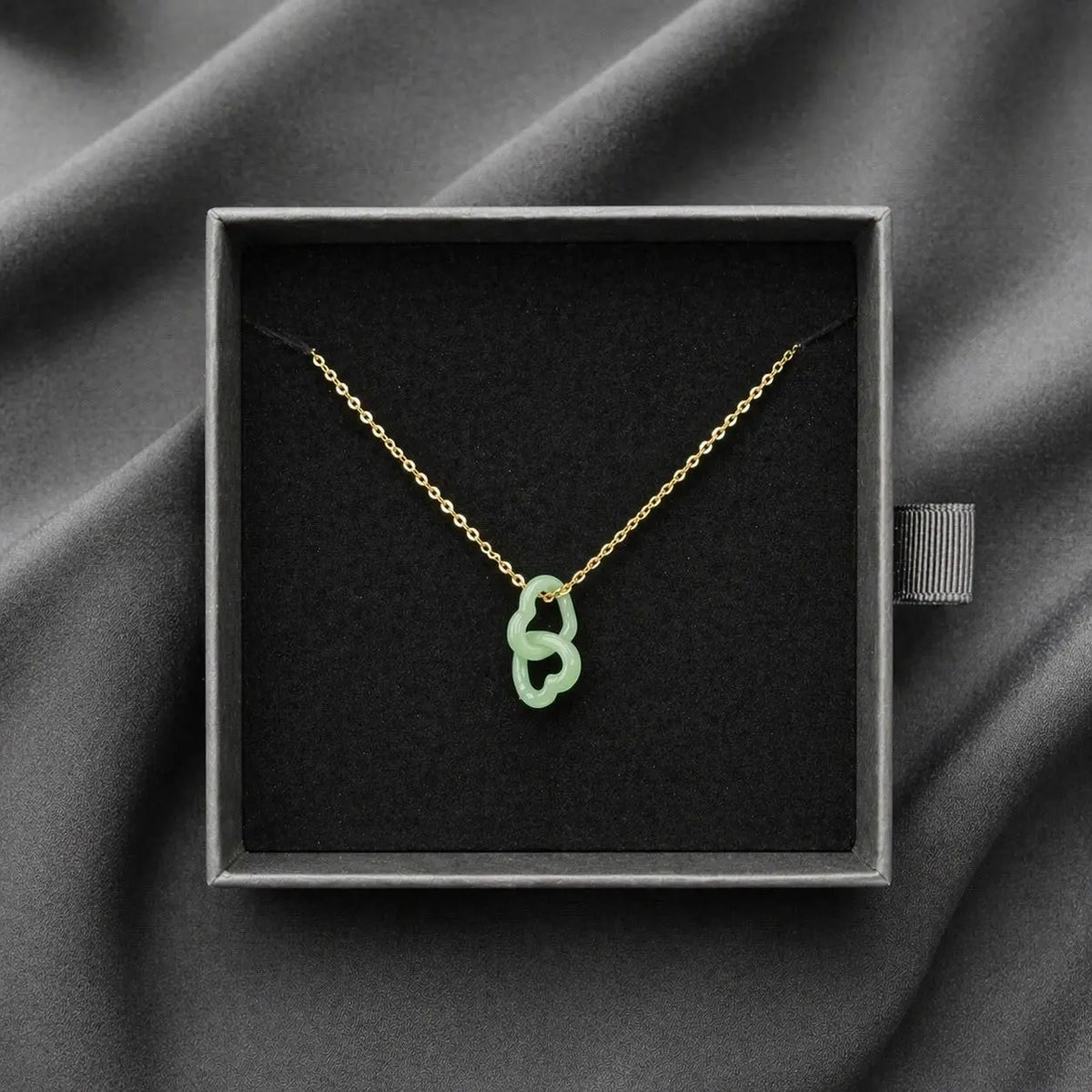 Necklace with a green pendant in a black box on a gray fabric background