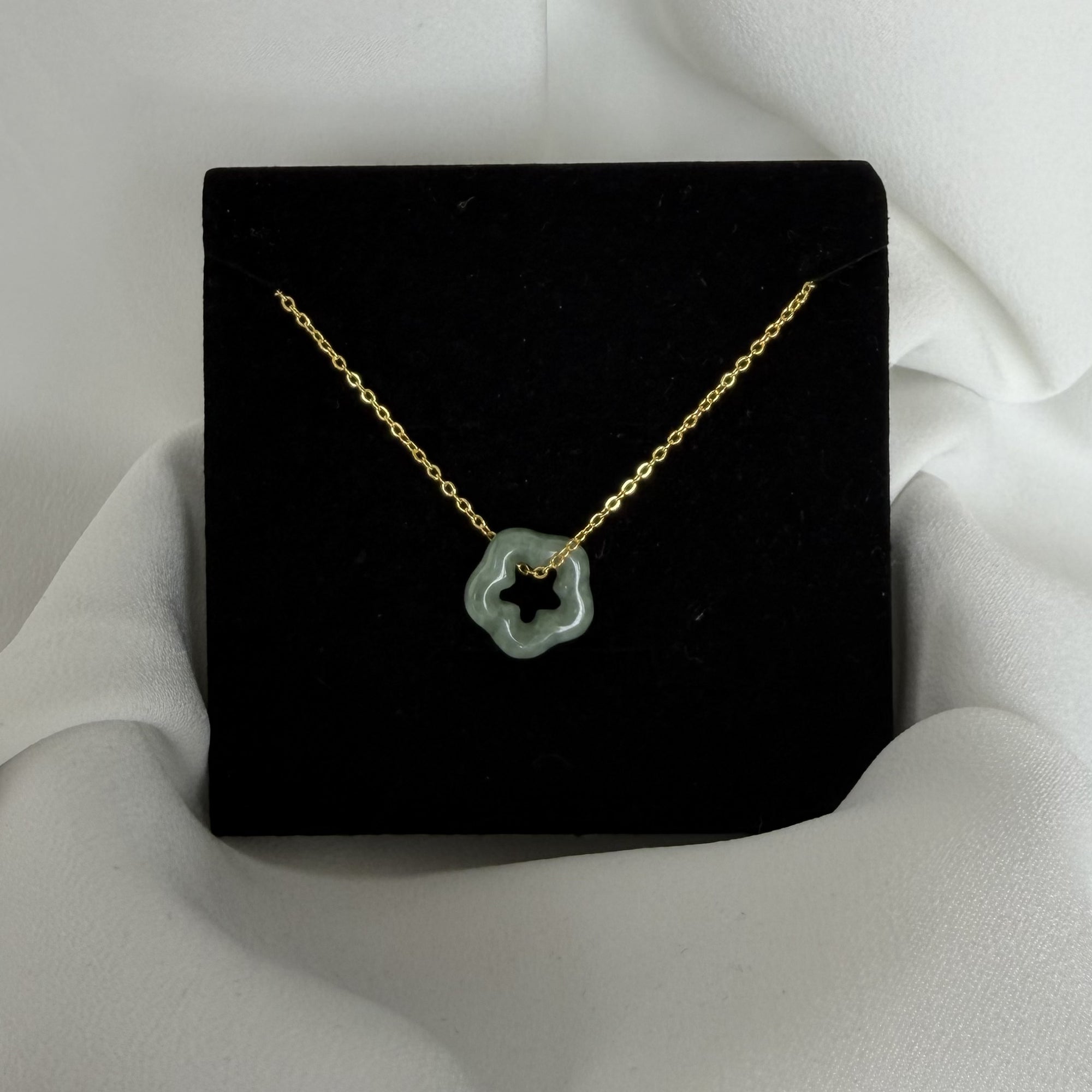 Gold necklace with a green pendant on a black stand against a white background